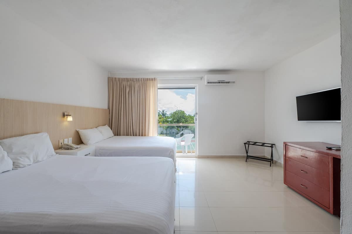 Habitación de hotel con dos camas, televisión, cómoda y balcón con vistas a la vegetación.
