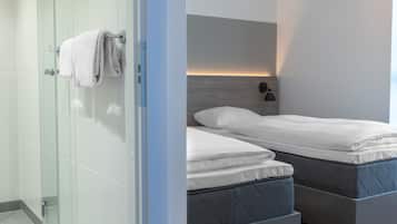 Un dormitorio moderno con dos camas, cabina de ducha de vidrio y mesita de noche con lámpara.