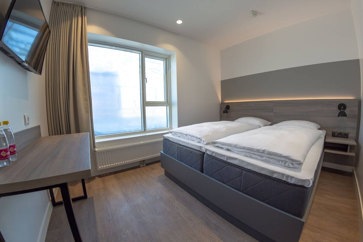 A modern hotel room with a large bed, a desk, and a TV mounted on the wall.