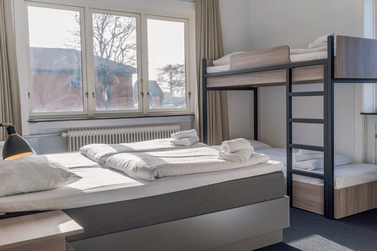 A bunk bed room with a window, a desk, and a radiator.