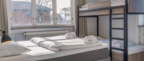 Une chambre avec un lit superposé, une fenêtre, un bureau et un radiateur.