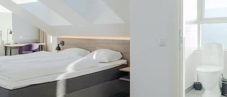 Un dormitorio moderno con un tragaluz, una cama, una mesita de noche y vistas al baño.