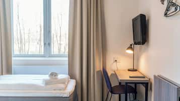 Une chambre d’hôtel avec un lit, un bureau avec une lampe, une télévision et une fenêtre avec des rideaux.
