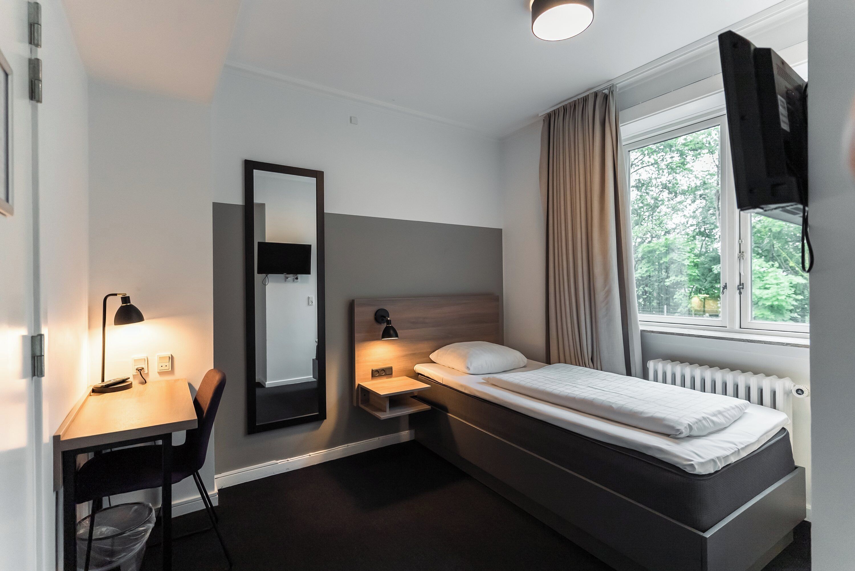 Une chambre d’hôtel moderne équipée d’un lit, d’un bureau, d’une chaise et d’une grande fenêtre avec des rideaux.