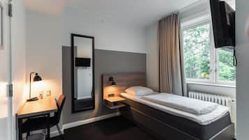 A modern hotel room with a bed, desk, chair, and a large window with curtains.