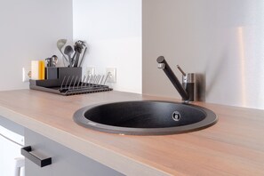A modern kitchen with a round black sink, stainless steel faucet, and a utensil holder with various kitchen tools. - Copenhagen Go Hotel (Kastrup)