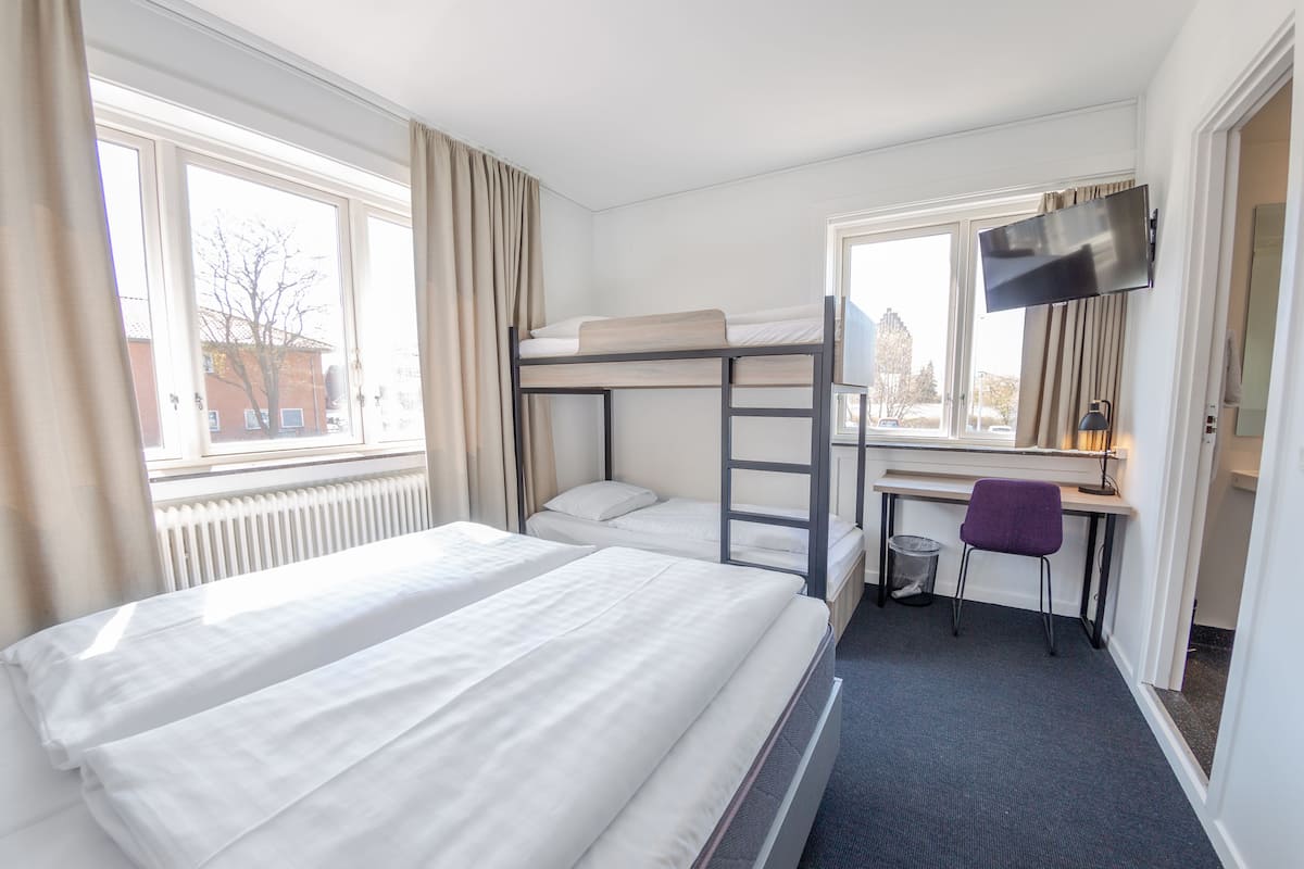 A hotel room with two beds, a desk, a chair, a TV, and a window with curtains.