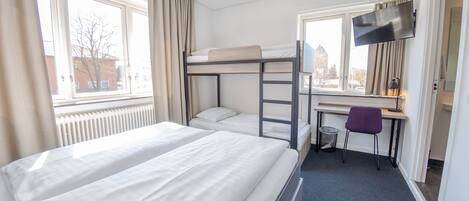Ett hotellrum med två sängar, ett skrivbord, en stol, en TV och ett fönster med gardiner.