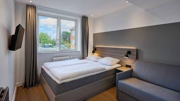 Ein modernes Hotelzimmer mit Bett, Sofa, Fernseher und einem Vorhangfenster.