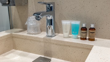 Un lavabo de salle de bain avec un robinet chromé, un sac en plastique, trois flacons de produits de toilette et un téléphone intelligent posés sur le comptoir.