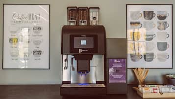 En kaffemaskin med en digital display, en affisch med en meny över olika kaffesorter och en vägg dekorerad med motiv av kaffekoppar.