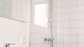 Un baño moderno con un lavamanos blanco, un espejo y una ducha con cabezal de ducha manual.