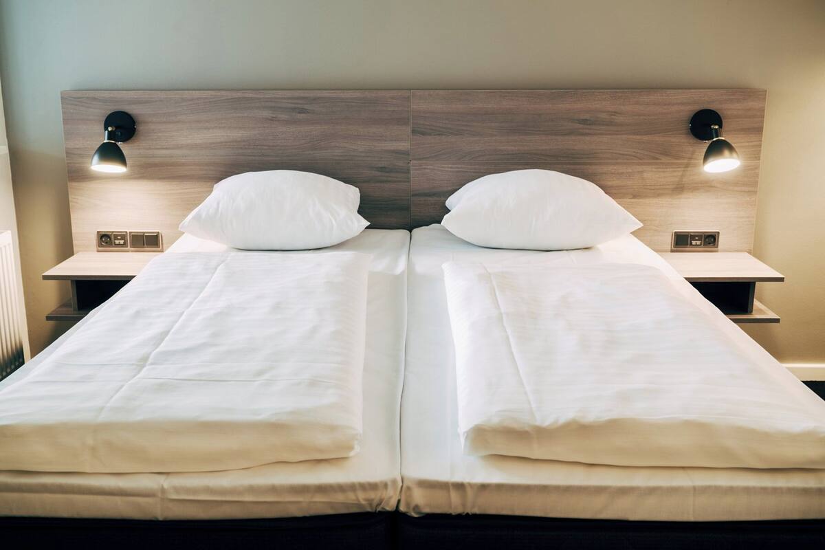 A double bed with white linens, two bedside tables with lamps, and a wooden headboard.