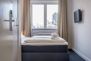 A hotel room with a bed, a TV mounted on the wall, and a window with curtains. - Copenhagen Go Hotel (Kastrup)