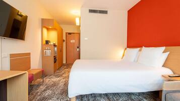 Habitación de hotel con cama, escritorio, televisión, kitchenette y una pared de acento roja.