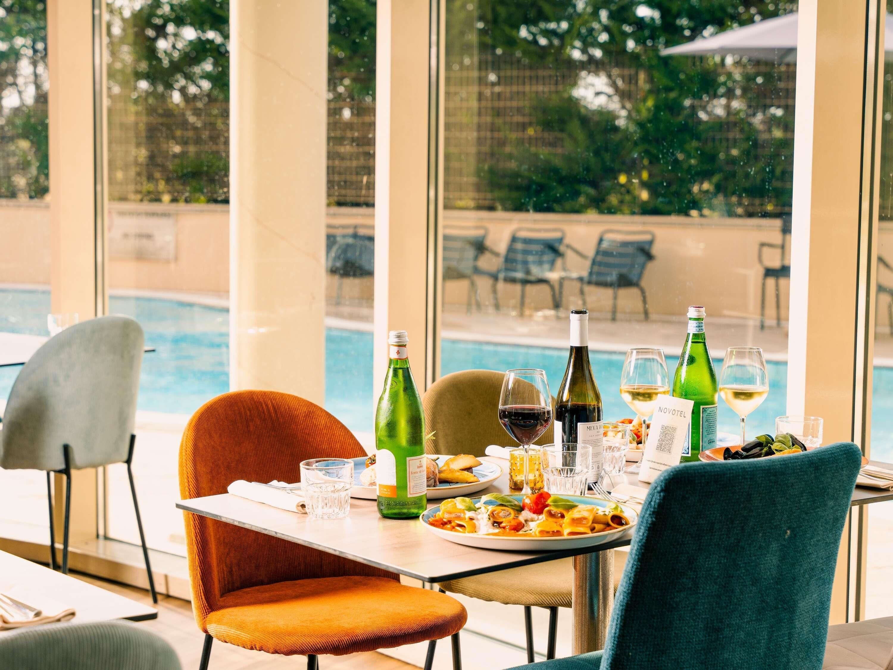 Una mesa de comedor con comida, copas de vino y botellas, con vista a una piscina.