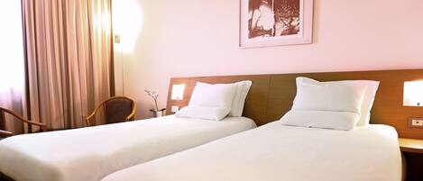 A hotel room with two beds, a wooden headboard, a chair, a vase with flowers, and a framed picture on the wall.