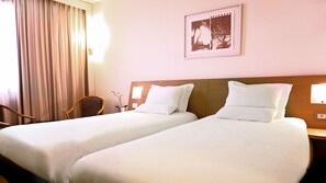 A hotel room with two beds, a wooden headboard, a chair, a vase with flowers, and a framed picture on the wall. - Novotel Roma Est (Rome)