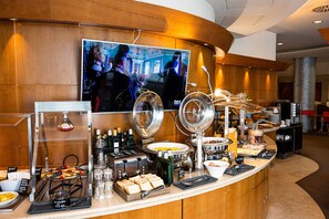 A breakfast buffet with various food items, a coffee station, and a television displaying a program. - Novotel Roma Est (Rome)