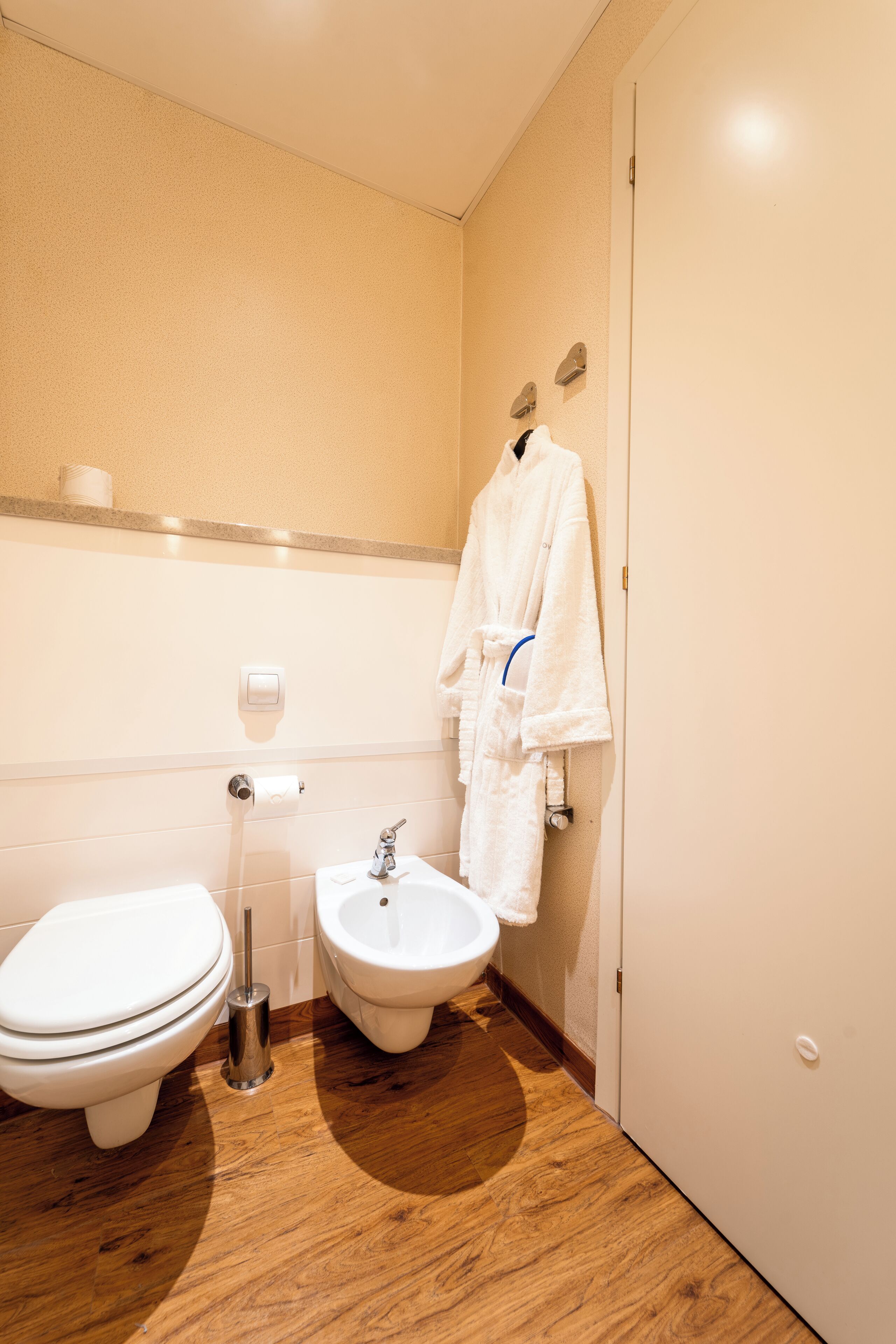 A bathroom with a toilet, bidet, and a robe hanging on the wall.