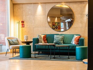 A modern lobby with a green sofa, a round table, and a chair. - Novotel Roma Est (Rome)