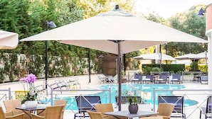 Un área de piscina al aire libre con sillones de descanso y sombrillas, rodeada de vegetación.