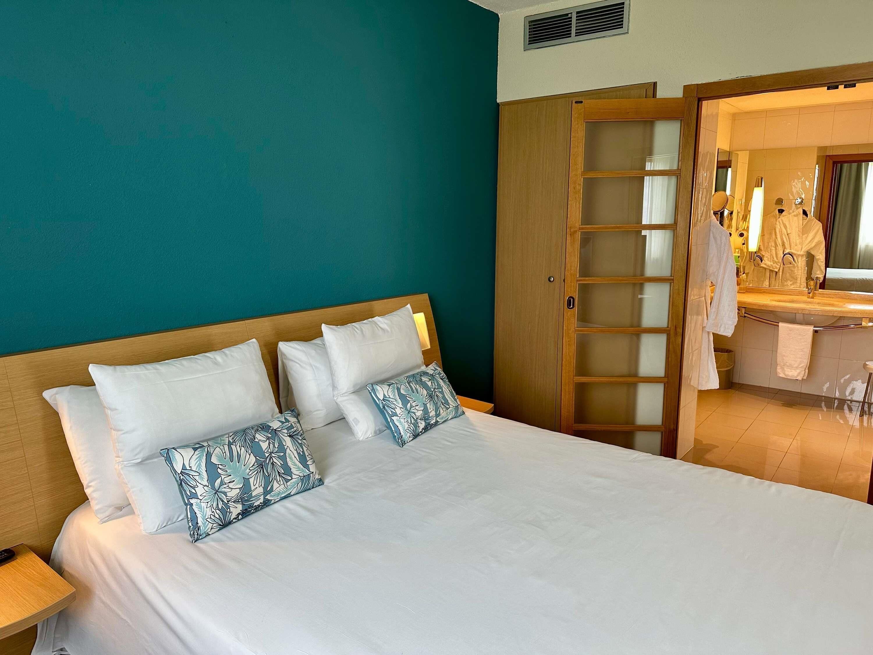 A hotel room with a bed, a nightstand, a bathroom with a mirror, and a wardrobe.