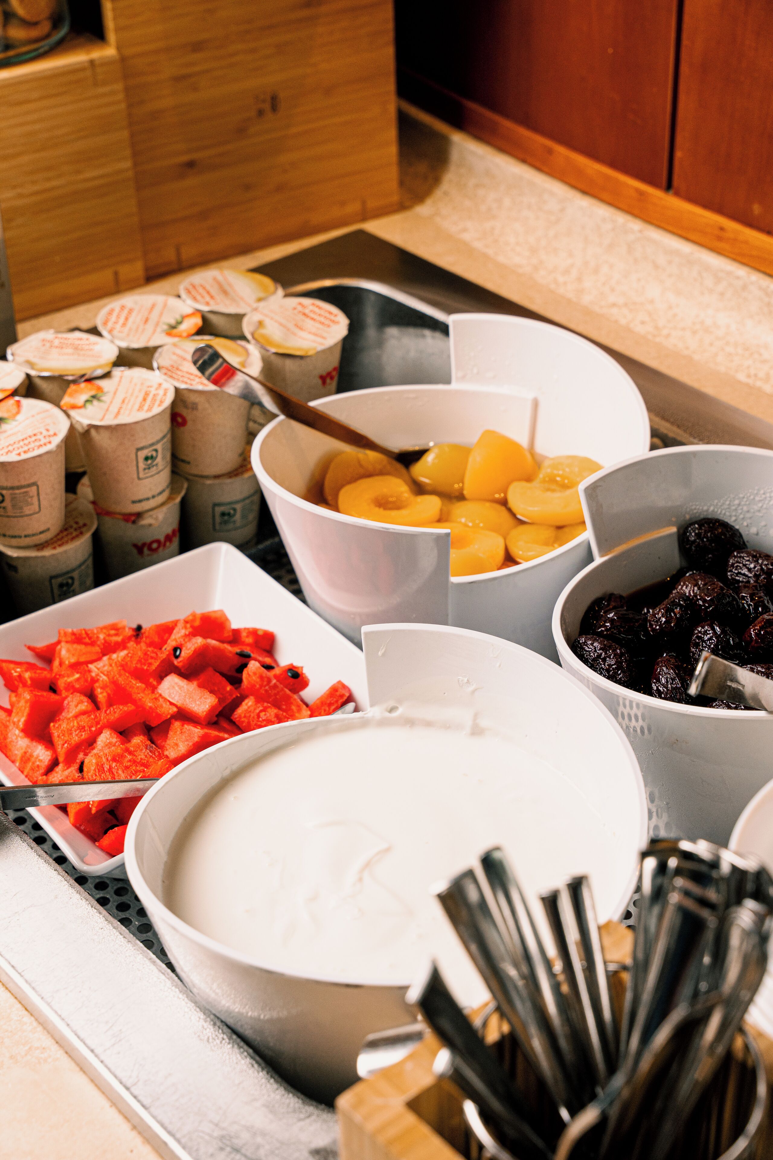 Un bufé con diferentes opciones de comida, incluyendo frutas cortadas y un tazón grande de sopa.