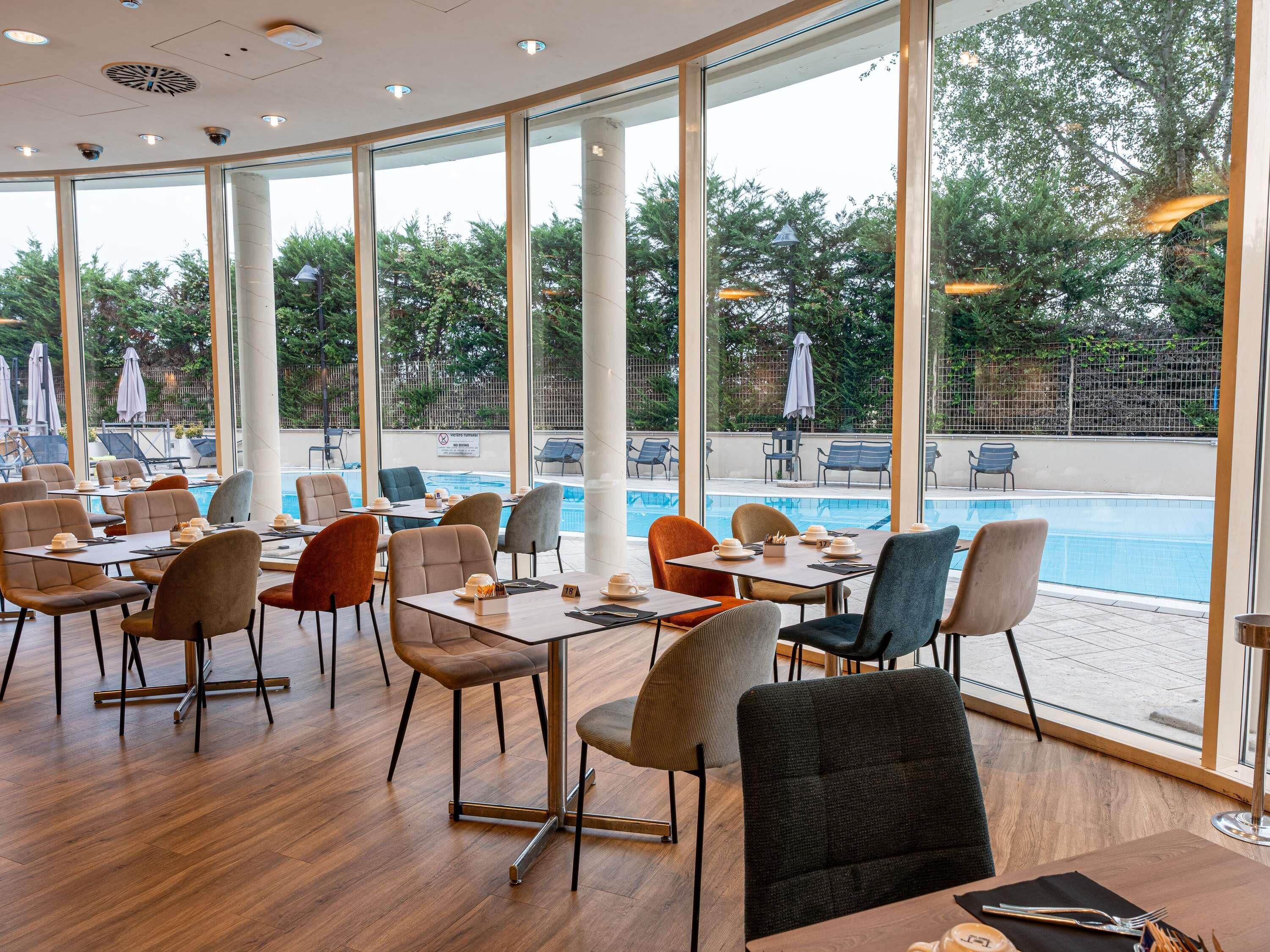 A restaurant with a pool view, featuring modern furniture and large windows.