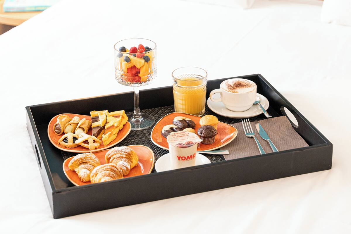 A breakfast tray on a bed with croissants, muffins, and fruit.