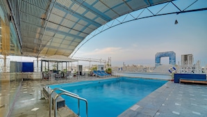 Piscina com área coberta, cadeiras de descanso e vista para o horizonte urbano.
