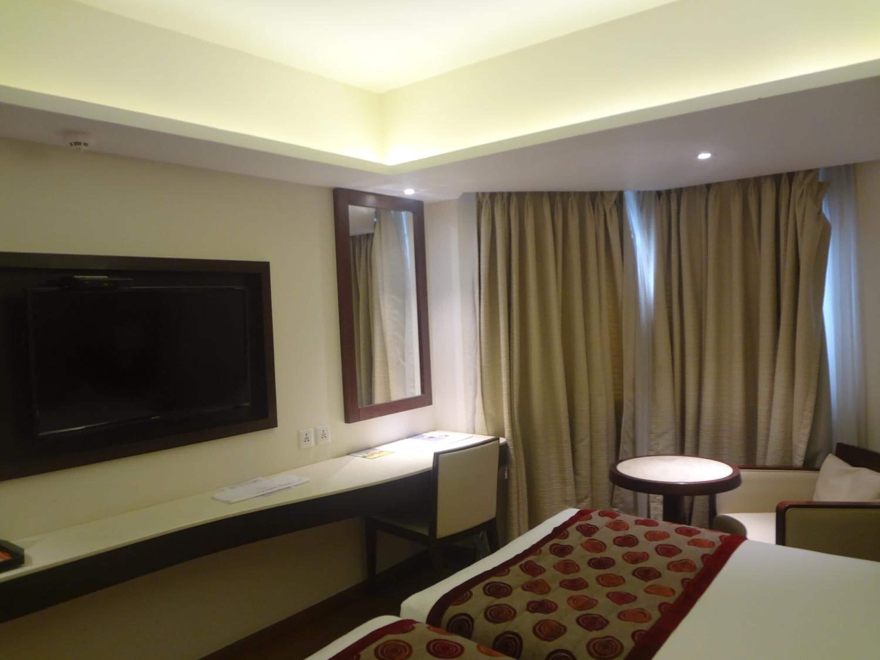 Habitación de hotel con cama, escritorio, silla, televisión y ventana con cortinas.