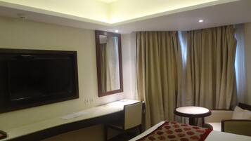 A hotel room with a bed, a desk, a chair, a television, and a window with curtains.
