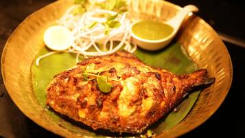 A plate with a grilled fish, sliced onions, and a green sauce.