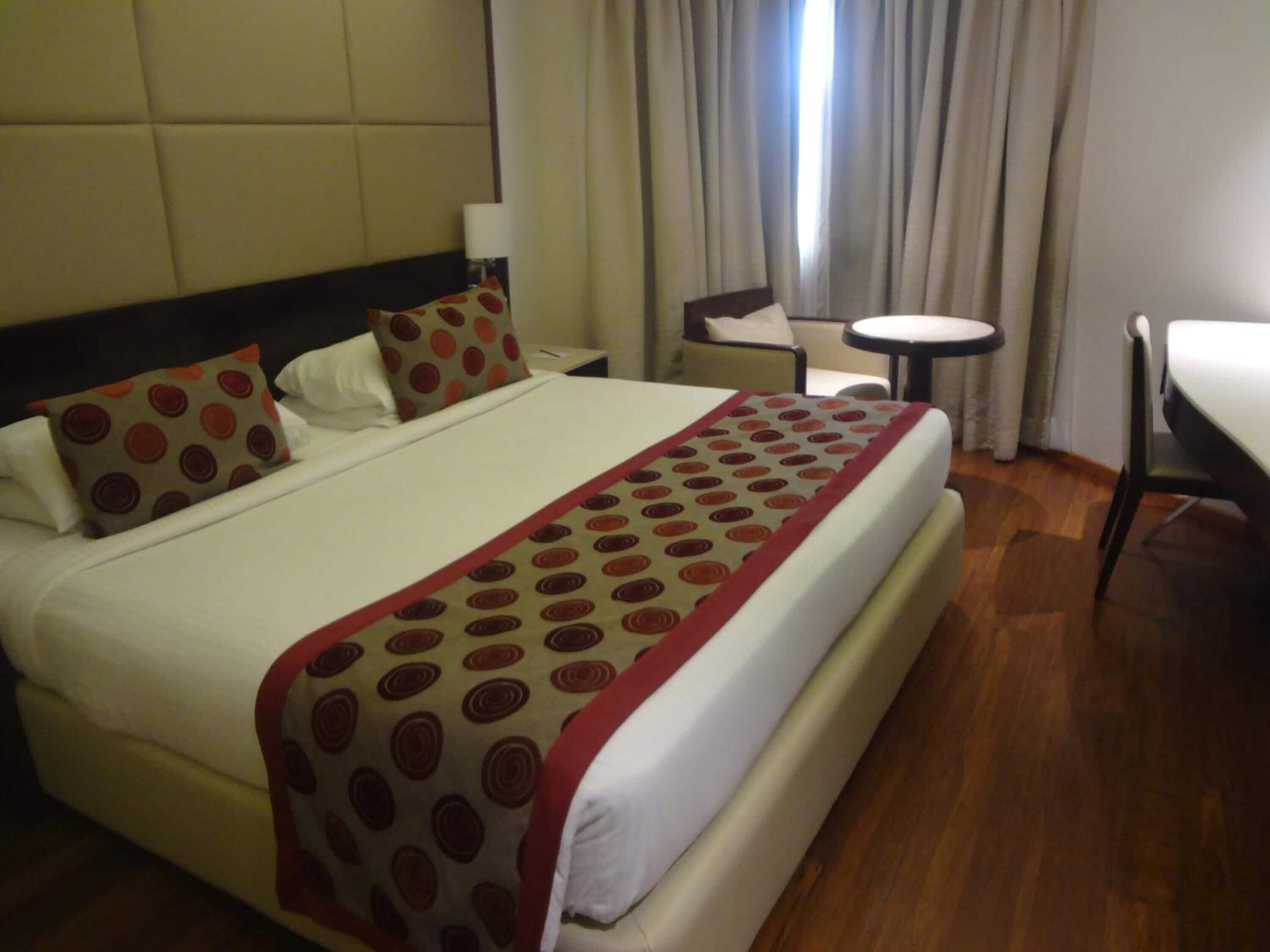 Una camera d'albergo con un letto grande, un comodino, un piccolo tavolino rotondo e una sedia.