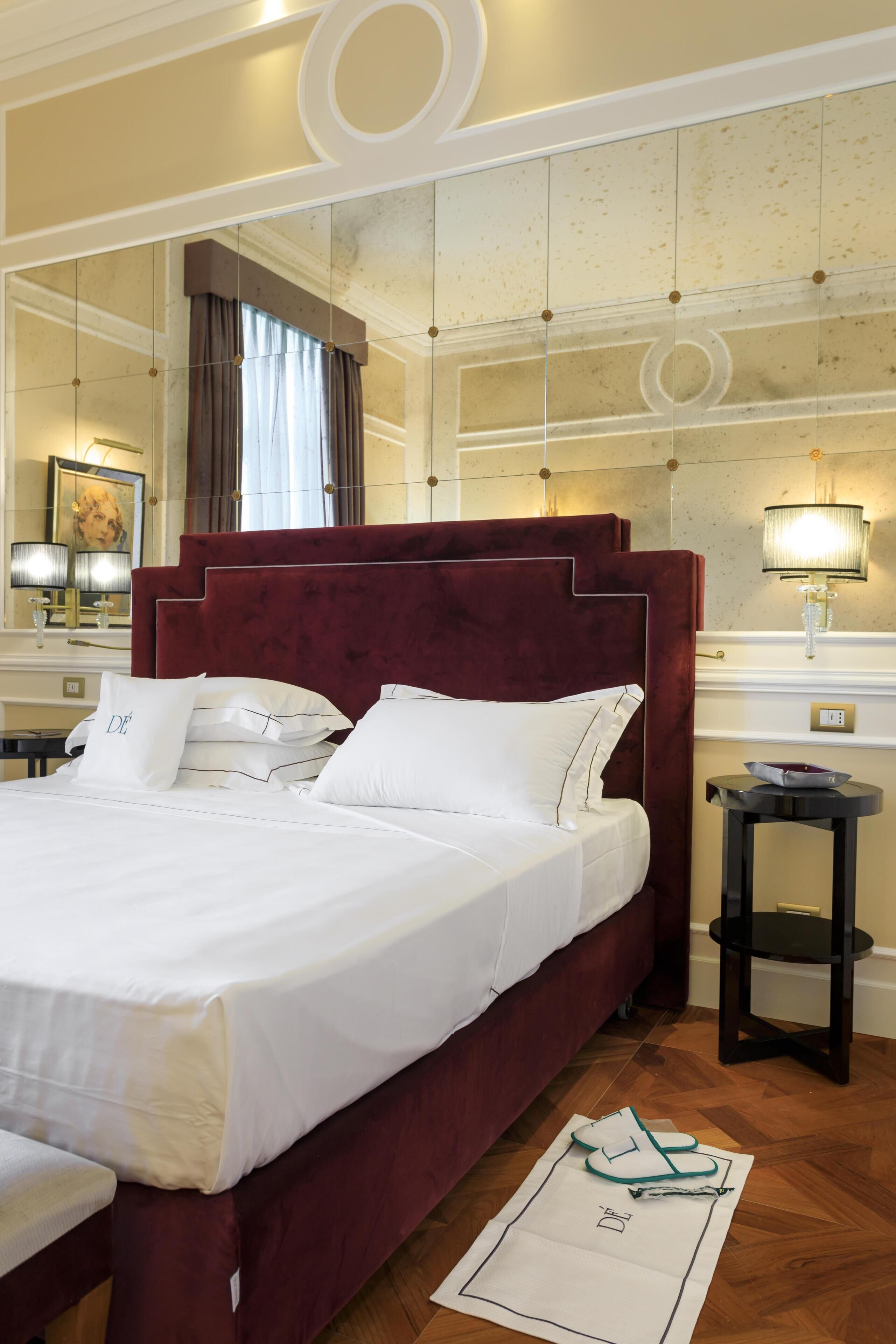 A hotel room with a large bed, a mirror, a nightstand, and a lamp.