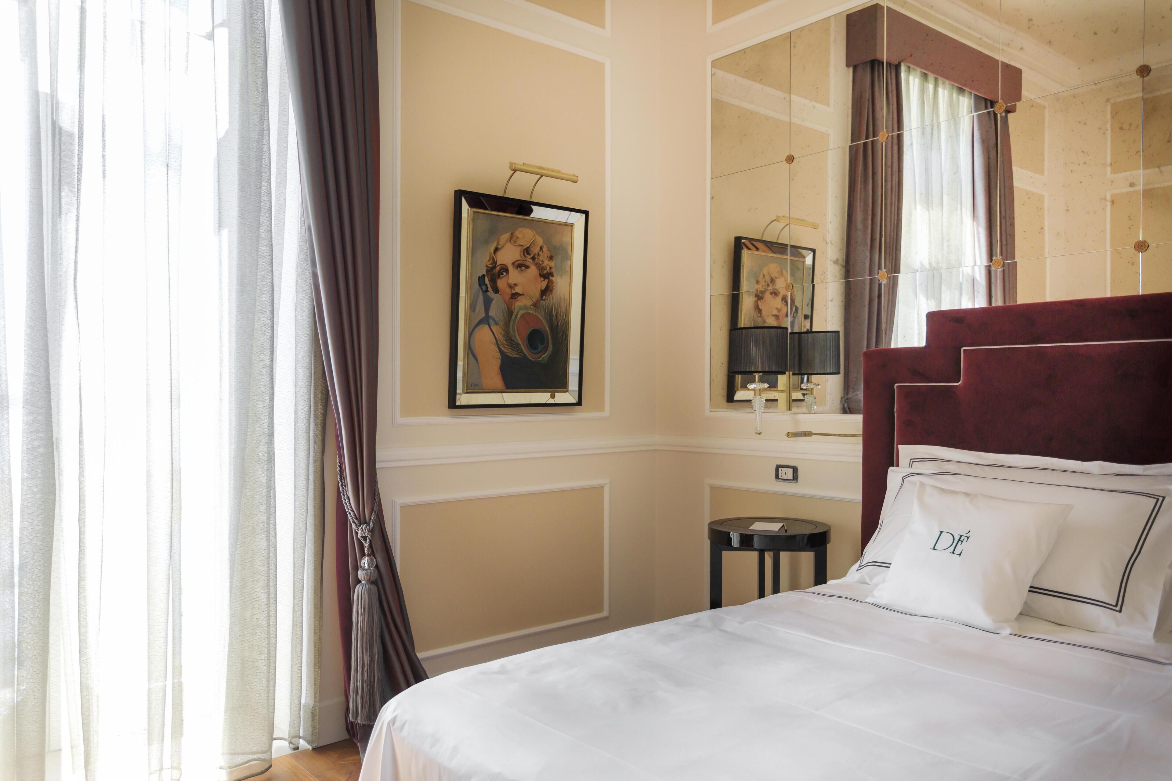 A hotel room with a large bed, a mirror, a painting on the wall, and a window with curtains.