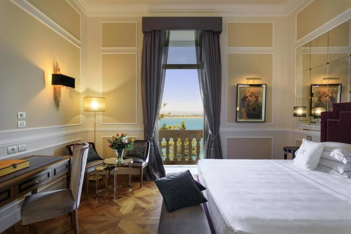 A hotel room with a bed, desk, chair, and a balcony with a view.
