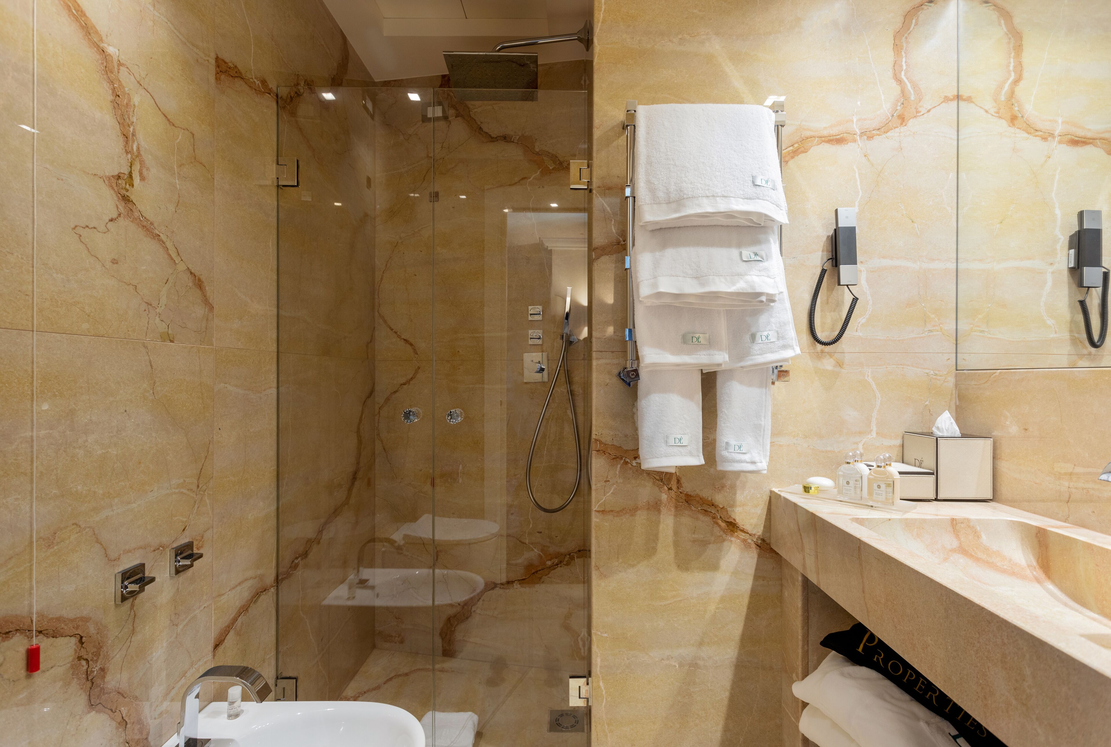 A bathroom with a glass-enclosed shower, a marble wall, a sink with a towel rack, and a mirror.
