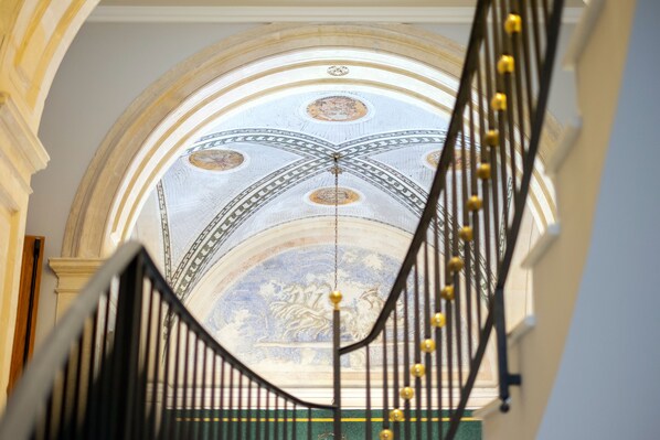 Una imponente escalera con vistas a un techo ornamentado y un candelabro.