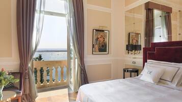 Une chambre d’hôtel avec un grand lit, une vue sur la mer, un balcon avec une balustrade et un bureau agrémenté d’une plante.