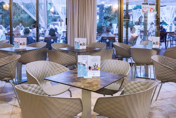 A restaurant with glass tables and cushioned chairs, menus on the tables, and a view of the outdoor seating area.