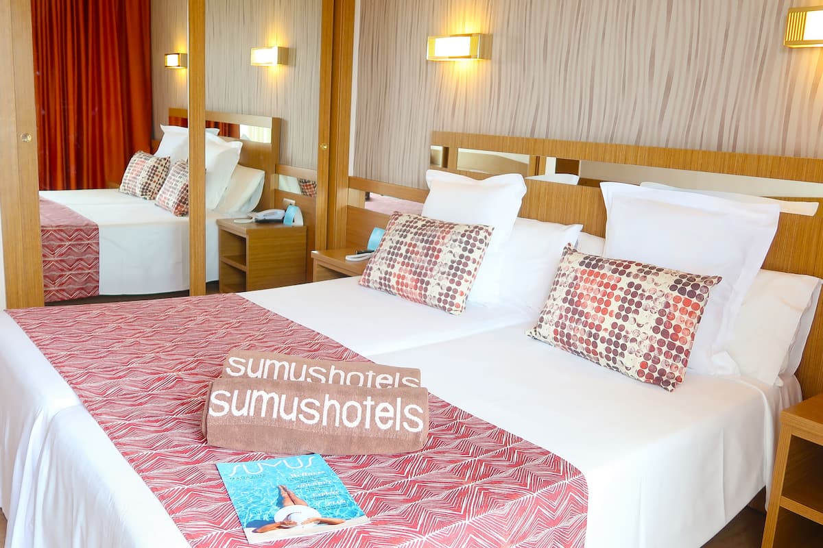 A hotel room with a large bed, two bedside tables, a mirror, and wall-mounted lights.