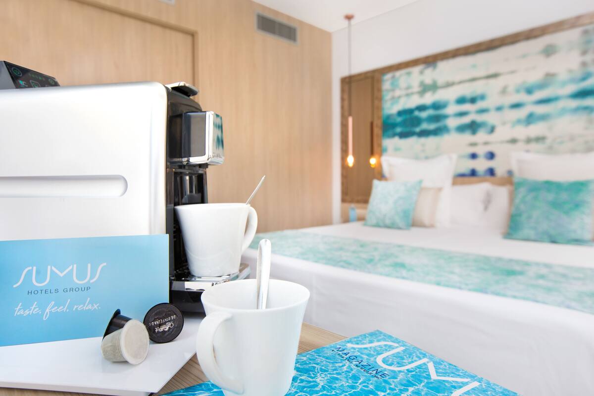A hotel room with a bed, a coffee machine, a cup, and a mug on a table.