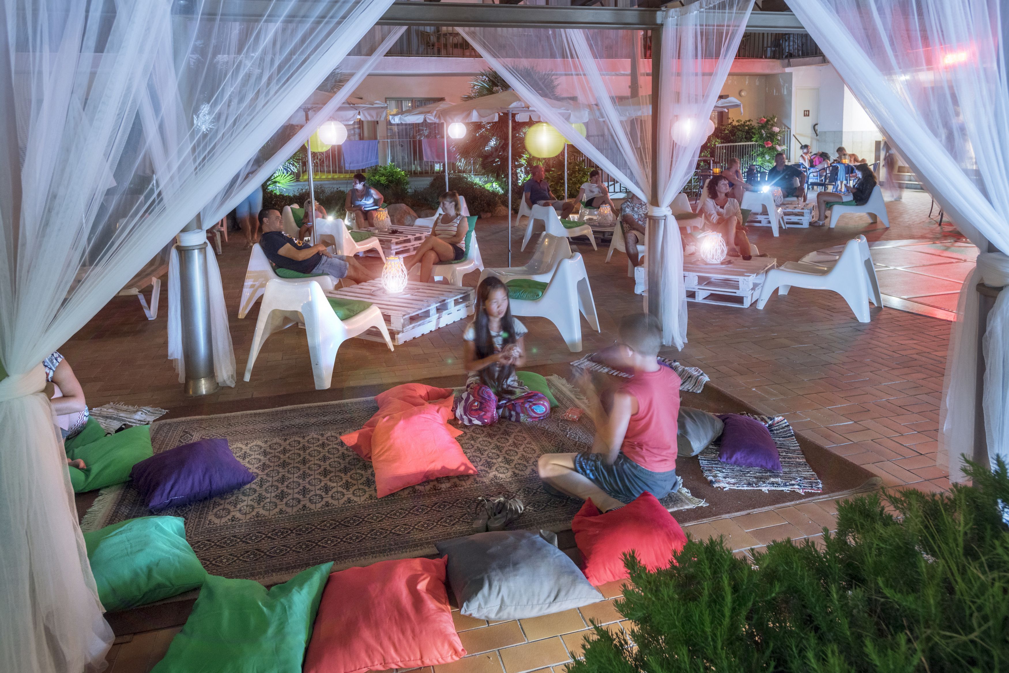 Un espace extérieur aménagé avec des chaises et des coussins blancs, sous une tonnelle drapée de voilages blancs.