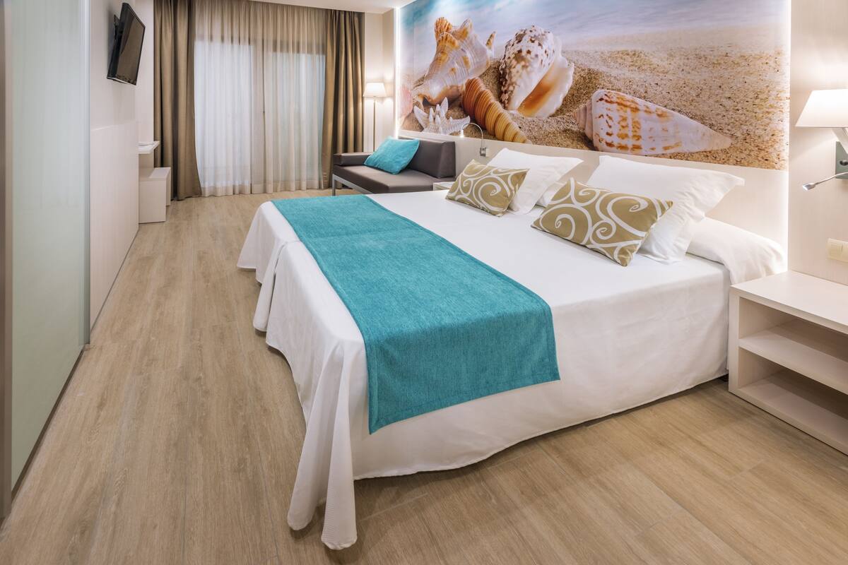 A hotel room with a bed, a desk, a chair, and a wall with a seashell mural.