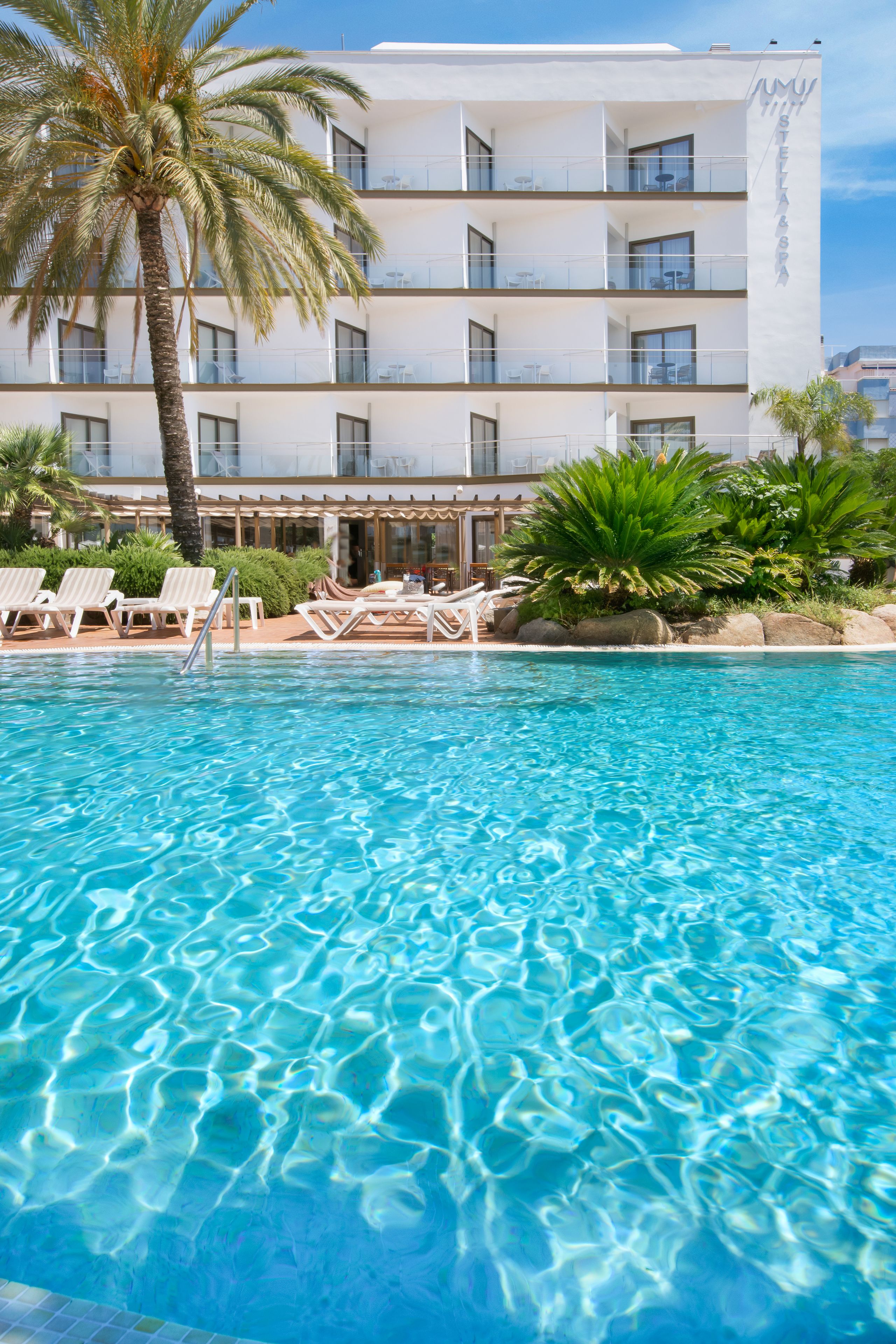 A hotel with a pool, lounge chairs, and palm trees.