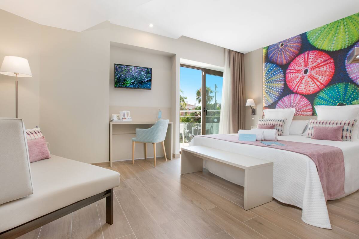 A modern hotel room with a large bed, a desk, a chair, and a TV.
