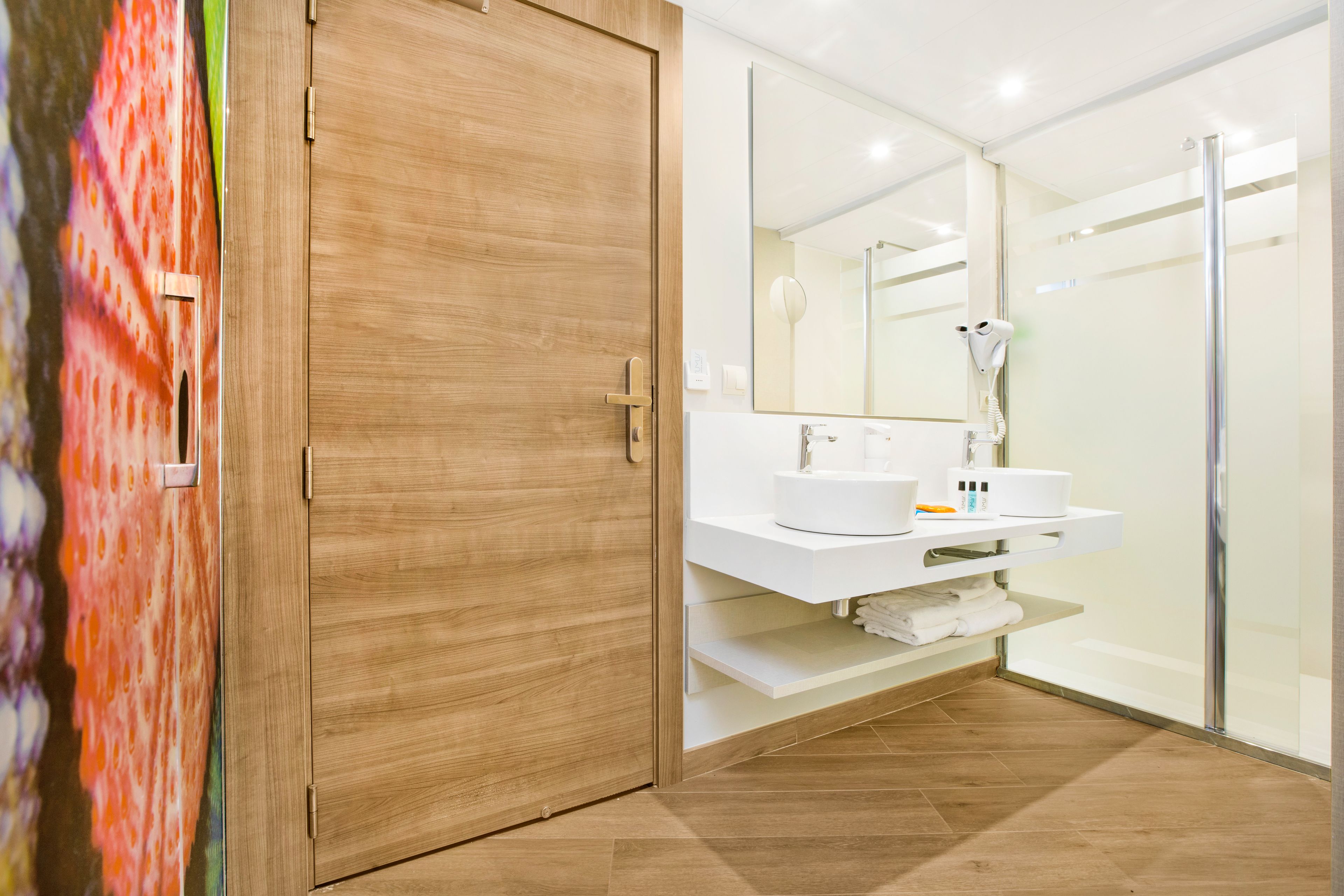 Un baño moderno con puerta de madera, lavamanos blanco y cabina de ducha de vidrio.