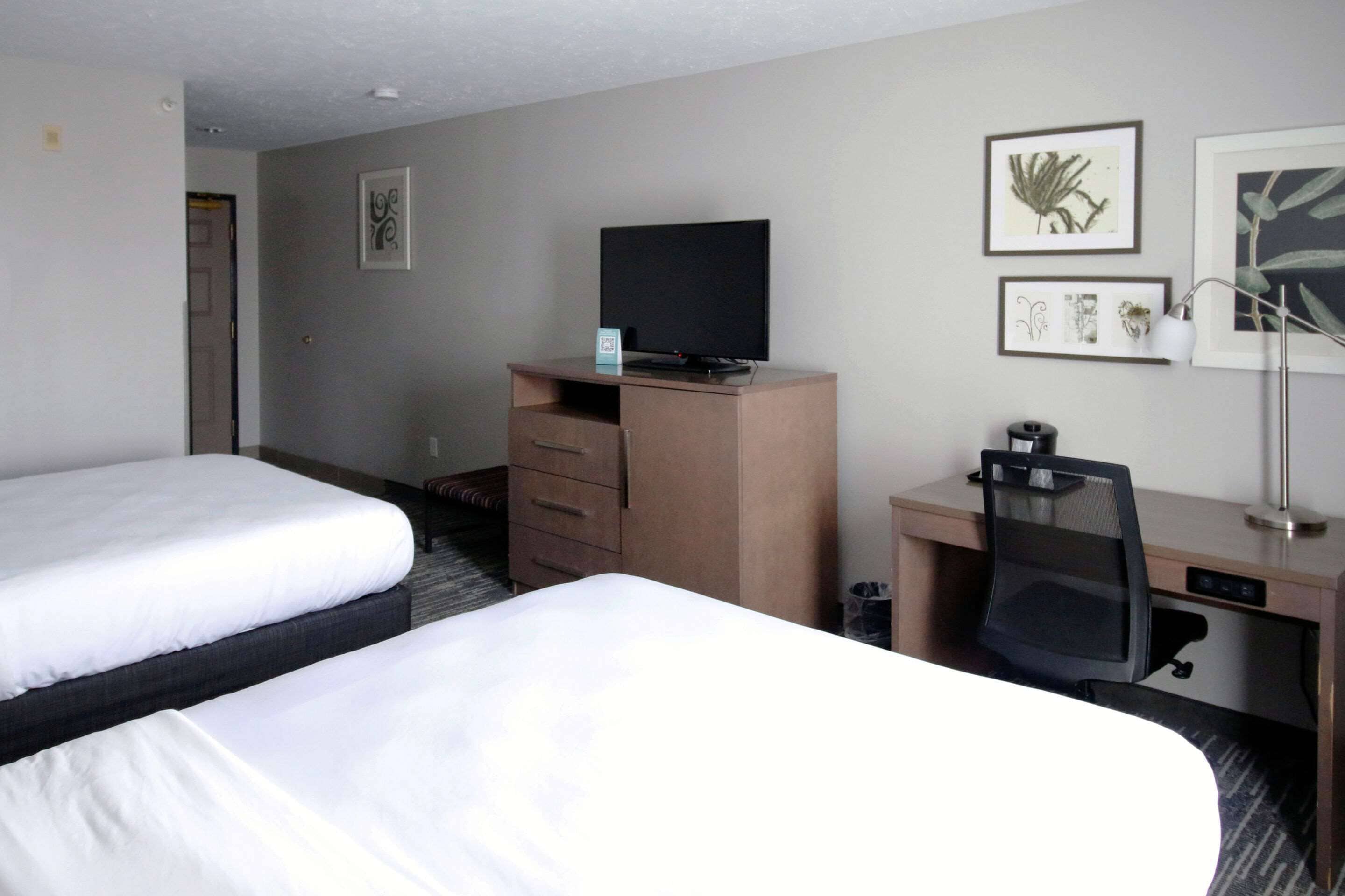A hotel room with two beds, a desk with a chair, a television, and framed artwork on the wall.